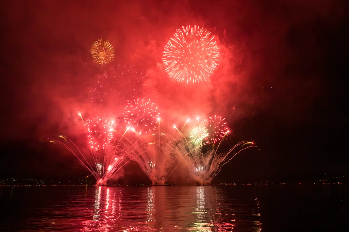 Das traditionelle Feuerwerk tauchte den See unter anderem in dramatisches Rot. Ein Feuerwerk am Nachthimmel erstrahlt in rot.